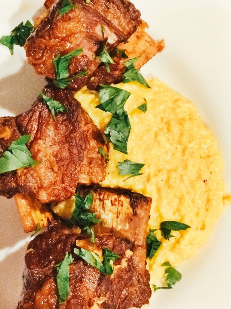 Browned short ribs and creamy polenta on a white plate with parsley on top