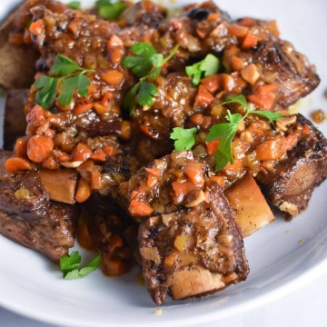 short ribs on a white plate sprinkled with carrots and parsley