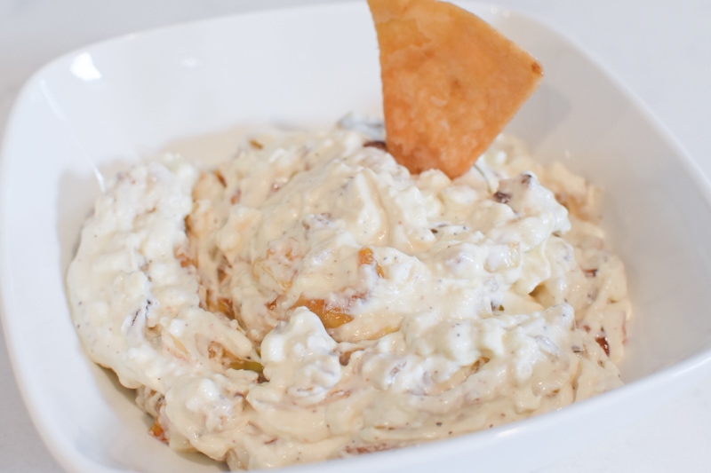 A white bowl of shallot dip with a pita chip dipping in