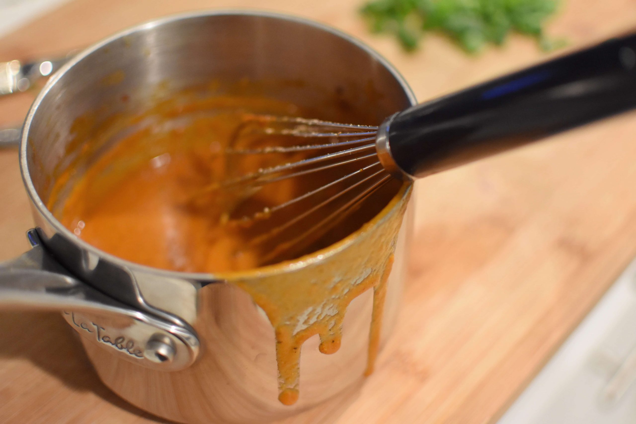 Red enchilada sauce being stirred with a whisk on a wood board.