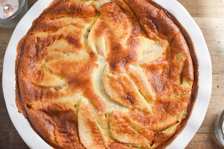 A white dish with pear clafoutis surrounded by candles