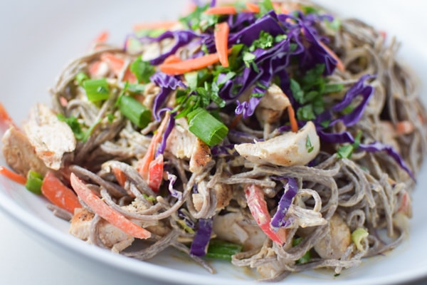 Soba noodles coated in a sunflower seed butter sauce topped with cilantro and carrots on a white plate