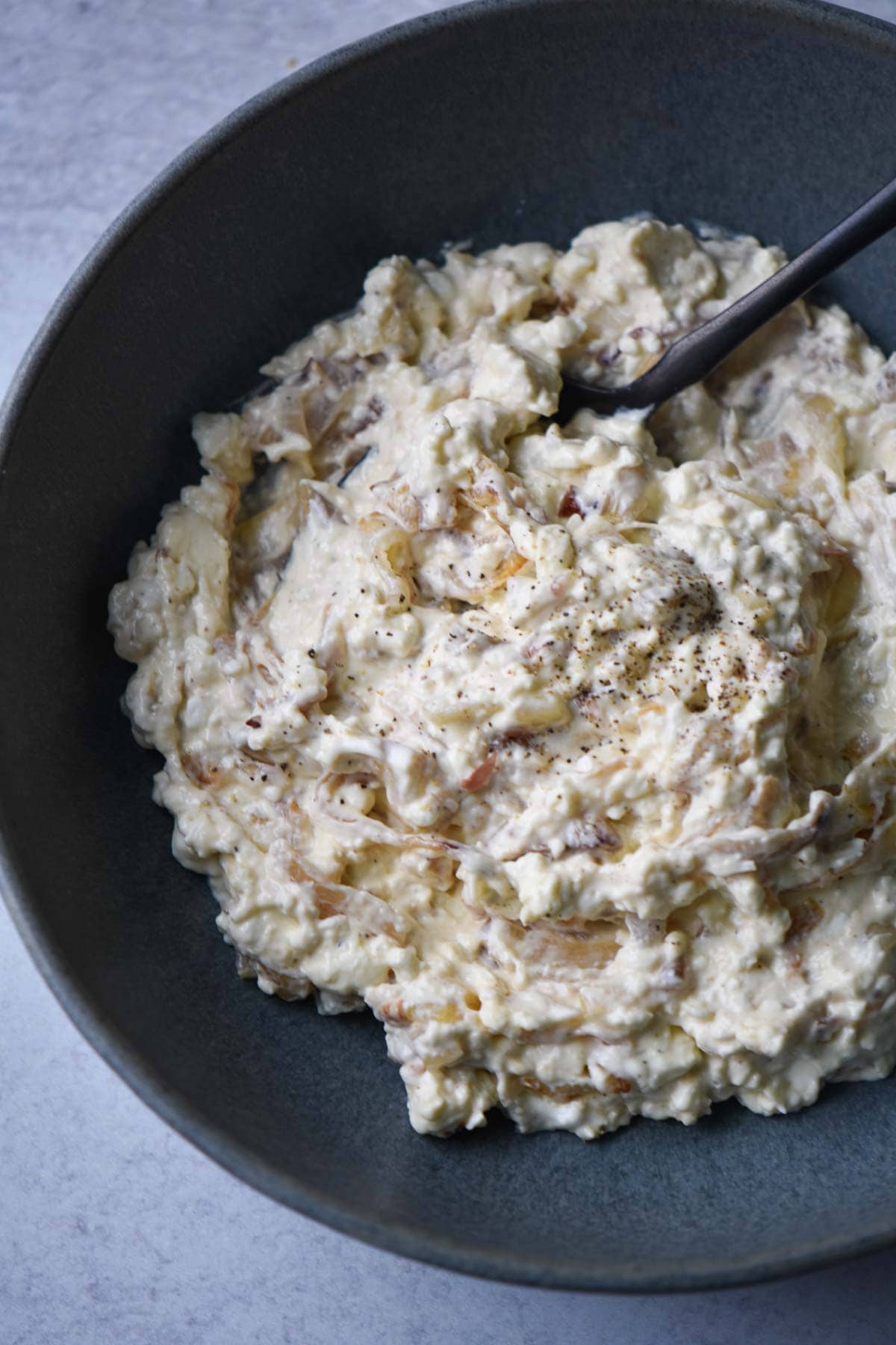 A creamy shallot dip in a black bowl with a black spoon dipping in