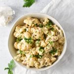 overhead shot of mac and cheese cauliflower in a white bowl with garlic and parsley