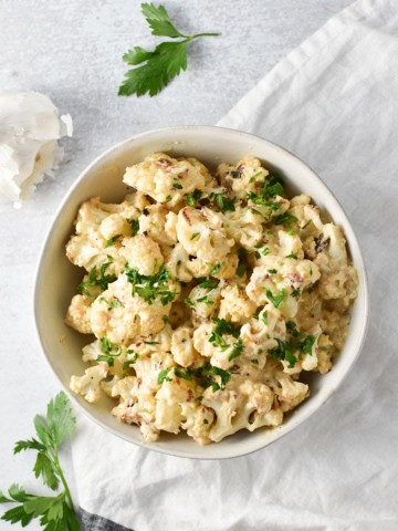 overhead shot of mac and cheese cauliflower in a white bowl with garlic and parsley