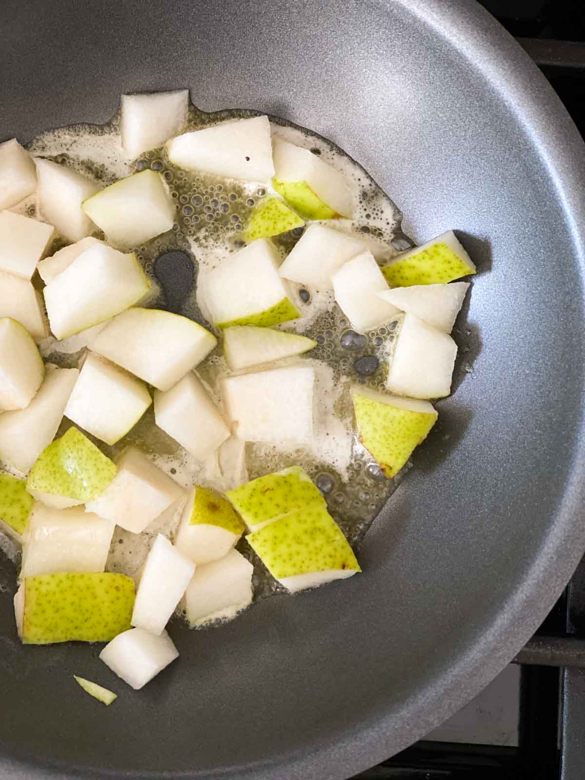 Adding chopped pears and butter or oil to a skillet to saute