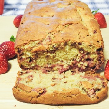 A cut slice of strawberry bread on a board with whole strawberries on the sides