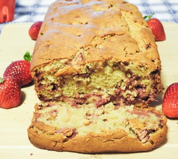 A cut slice of strawberry bread on a board with whole strawberries on the sides