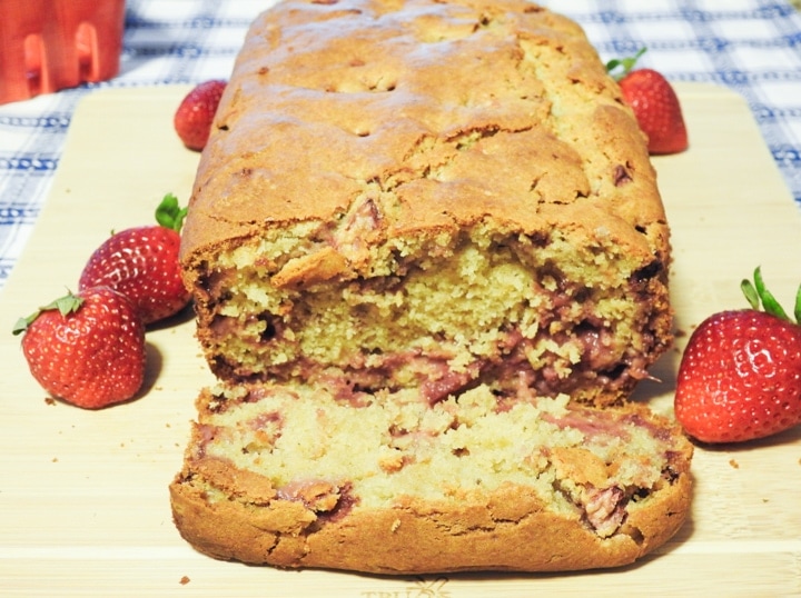 A cut slice of strawberry bread on a board with whole strawberries on the sides