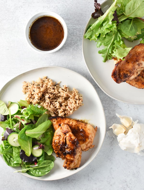 Two plates of garlic chicken with sauce, a simple salad, and rice