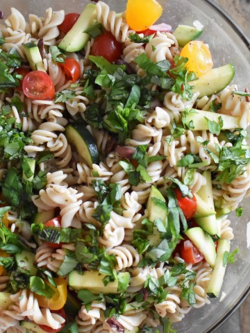 A bowl of gluten free pasta salad mixed with fresh vegetables on a wooden table