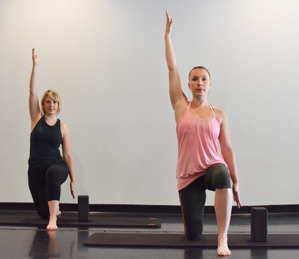 Two women demonstrating a quad and hip flexor stretch with restorative yoga for vestibular disorders