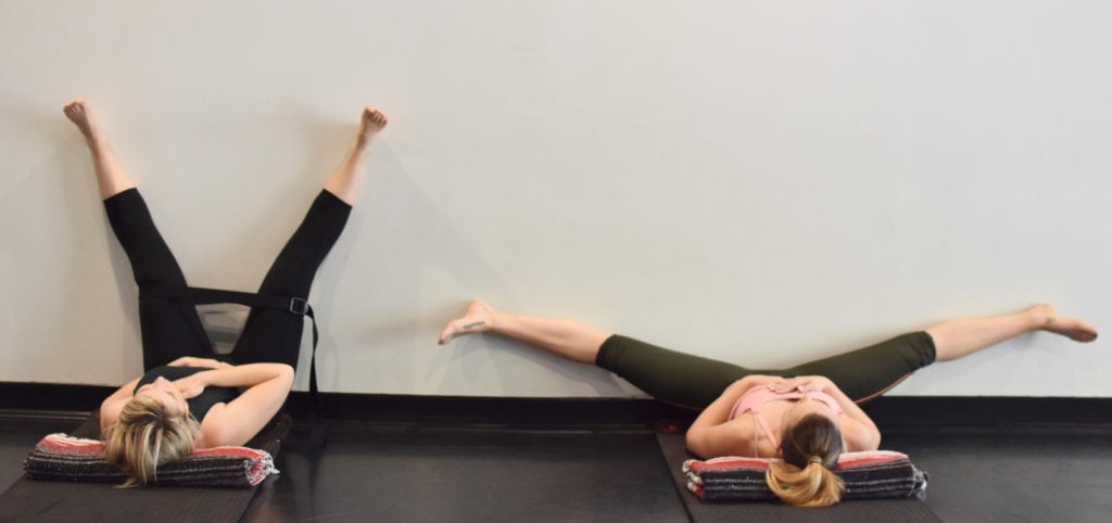 Two women lying on the ground with their legs up the wall for restorative yoga