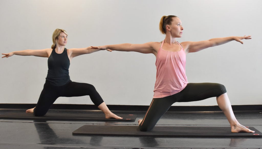 Two women practicing surfing warrior pose which is yoga for vestibular disorders