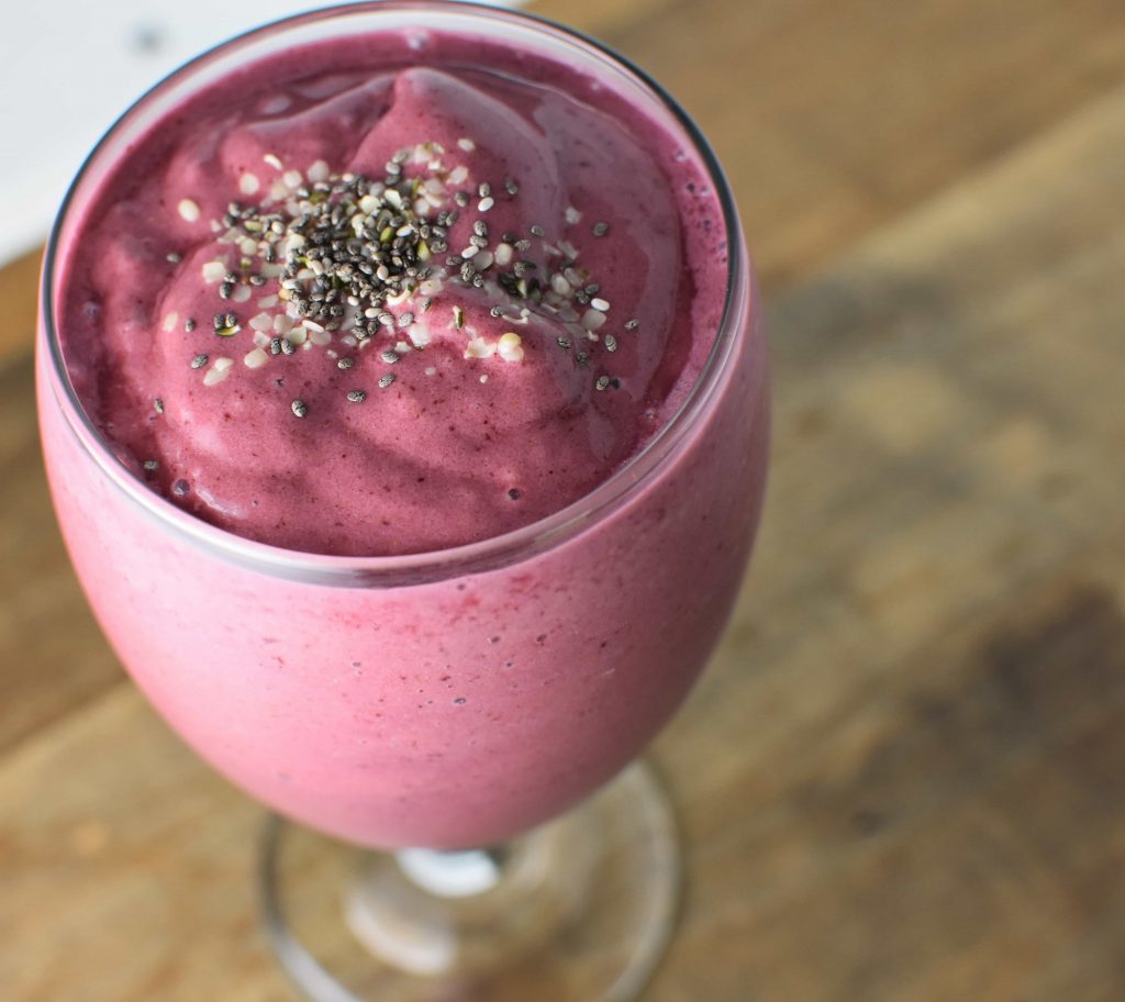 A cherry smoothie with hemp and chia seeds on top on a wood table
