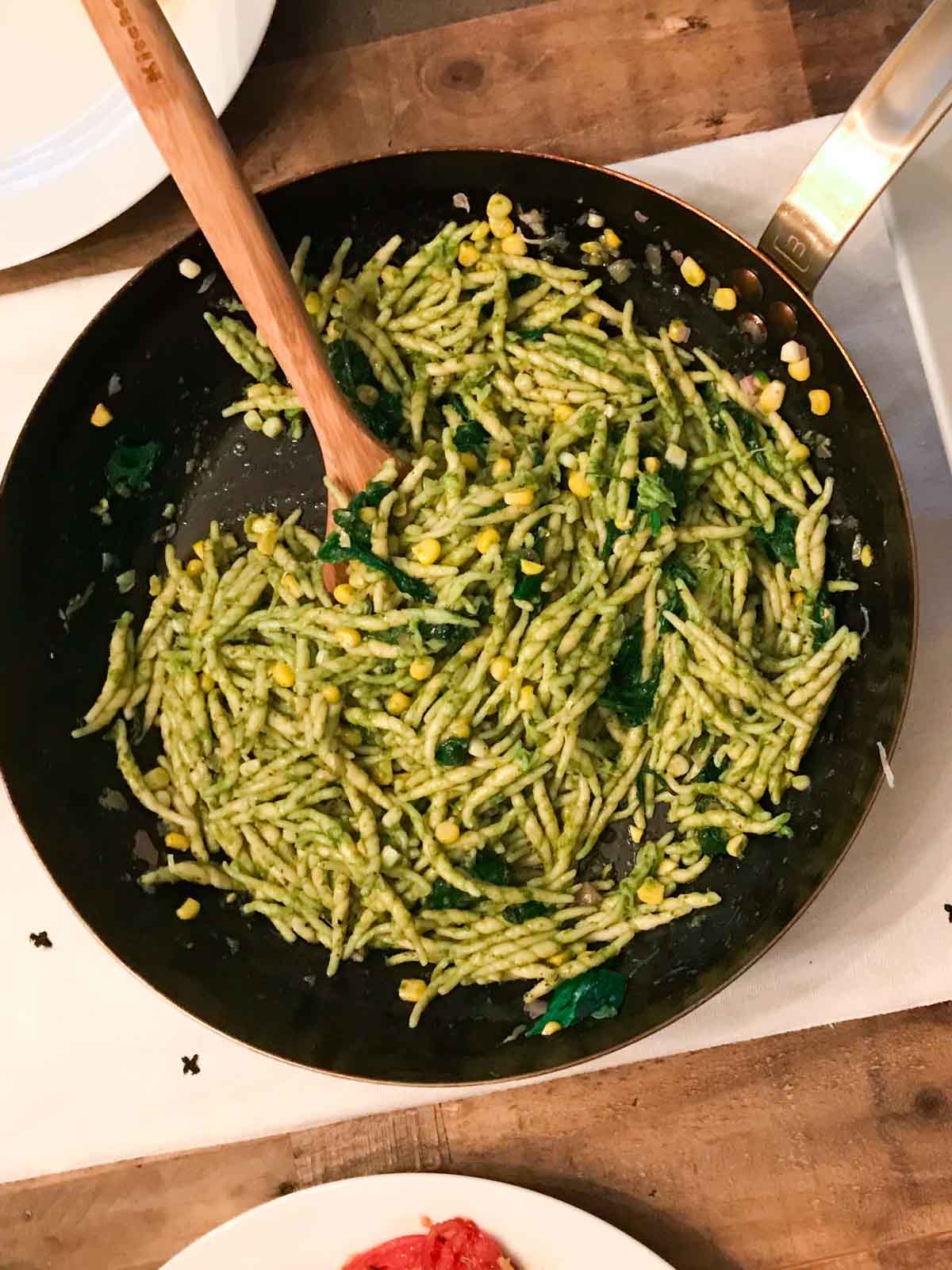 A pesto pasta in a pan on a wooden table with a serving spoon