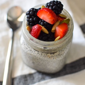 Chia seed pudding in a mason jar topped with seeds and strawberries next to a silver spoon