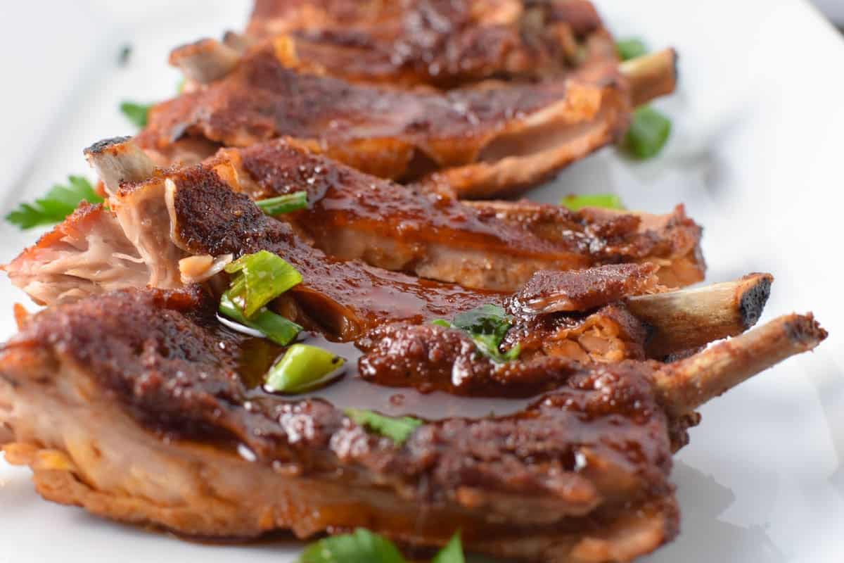 Baby back ribs lined up on a white plate, drizzled with BBQ sauce