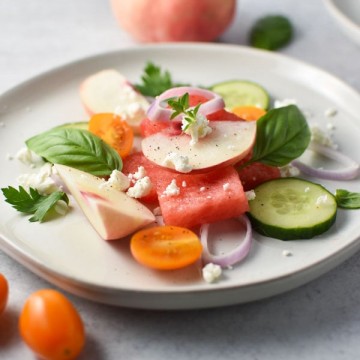 Watermelon, peaches, cucumber, goat cheese, and shallots mixed with fresh herbs on a plate