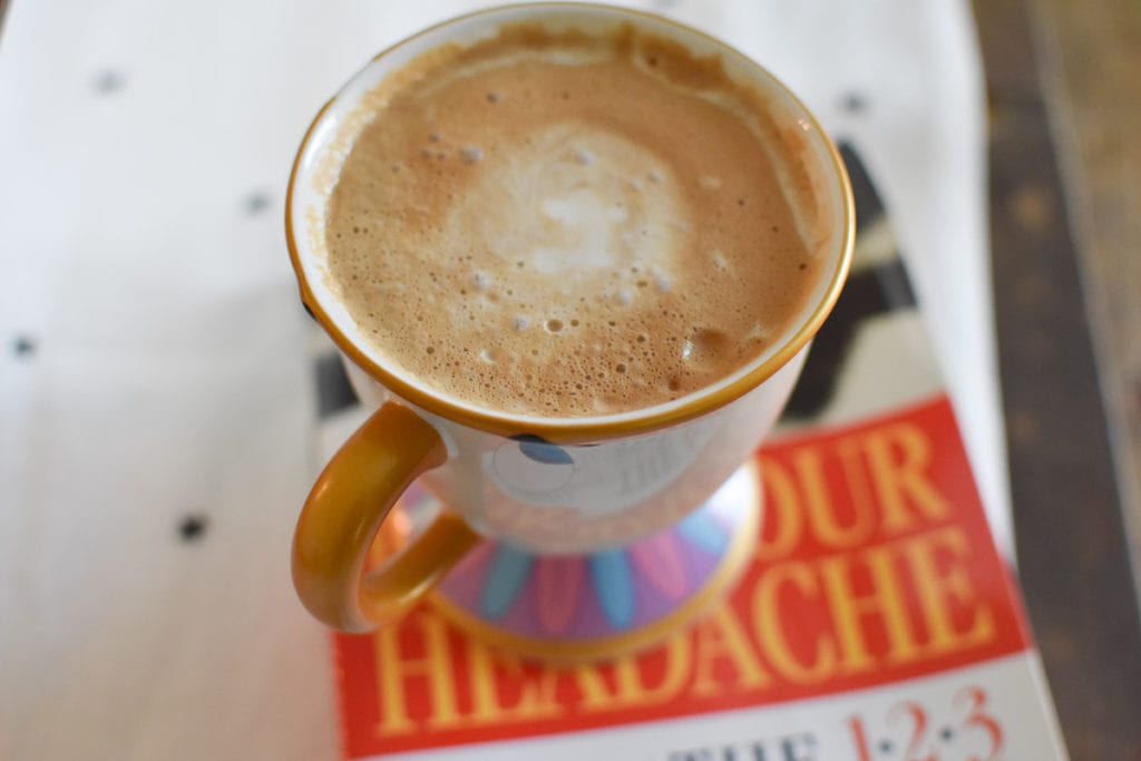 A cup of coffee in a Chip mug on top of Heal Your Headache. 