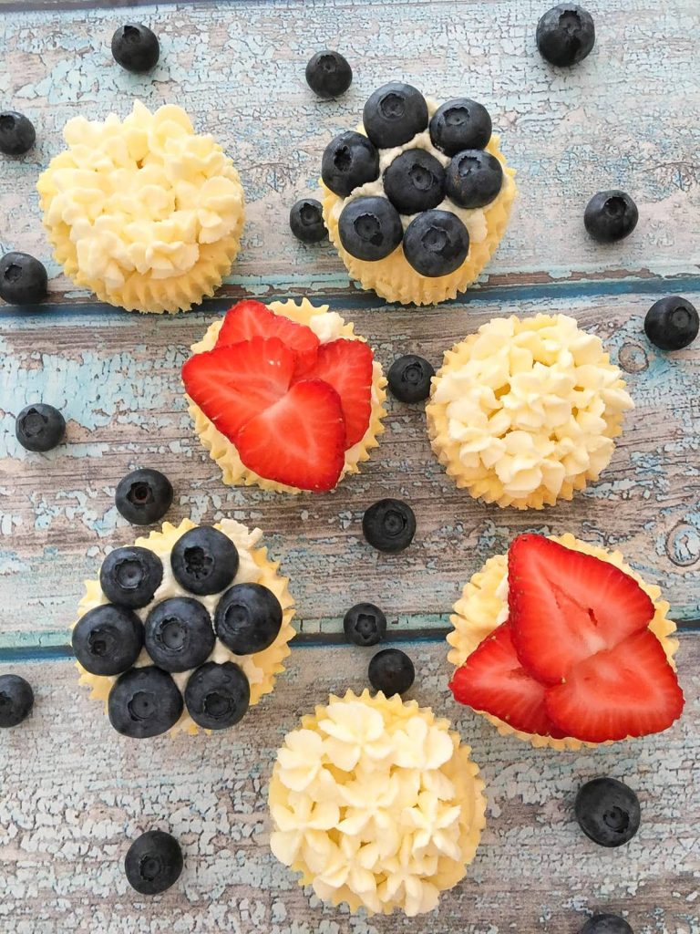 Cheesecake bites topped with frosting, strawberries and blueberries on a wooden background