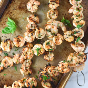 Grilled shrimp skewers on a baking sheet with parsley and basil