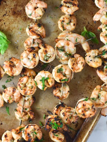 Grilled shrimp skewers on a baking sheet with parsley and basil