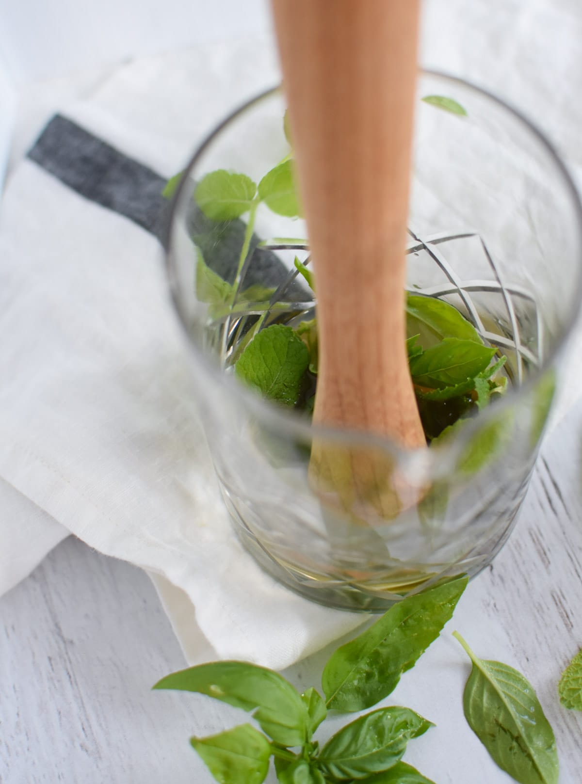 A muddler in a glass cocktail container smashing mint and basil in pear juice