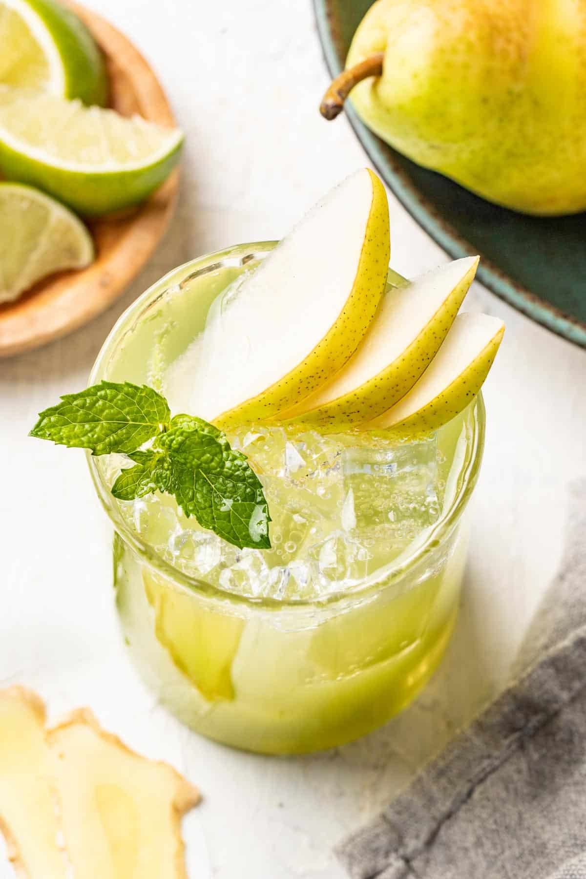 A sparkling pear mocktail in a glass with ice and sliced pears.