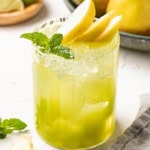 A pear mocktail topped with slice pears and fresh mint in a tall, clear glass with ice.