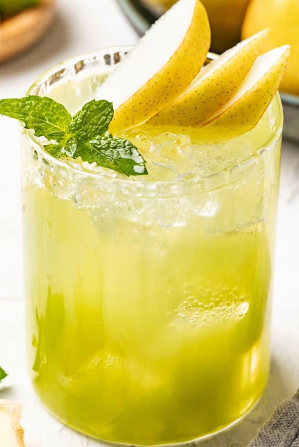 A pear mocktail topped with slice pears and fresh mint in a tall, clear glass with ice.