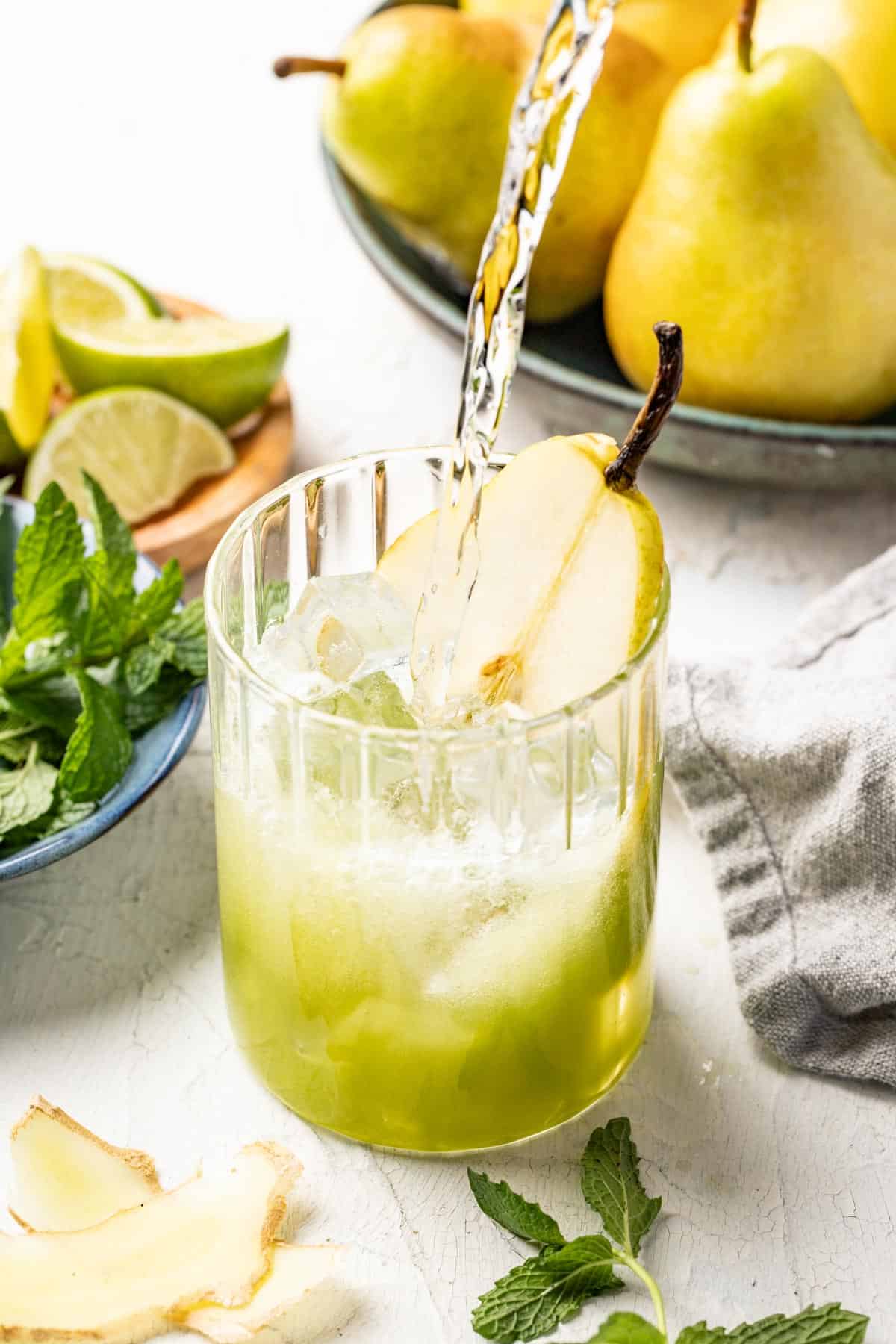 Pouring the club soda into the pear juice base in a glass with ice.