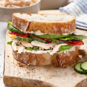 A sandwich with rotisserie chicken and Boursin cheese on a cutting board.