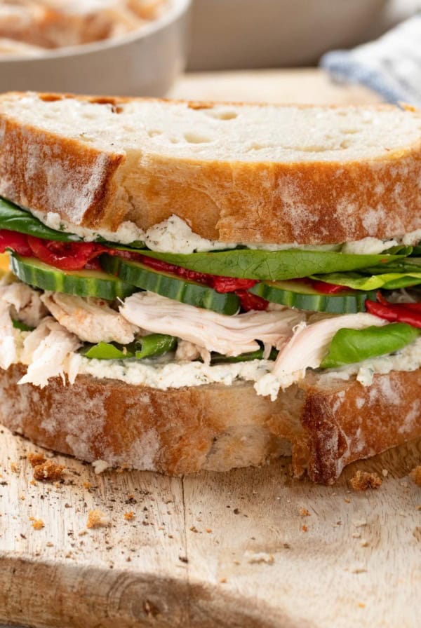 A sandwich with rotisserie chicken and Boursin cheese on a cutting board.