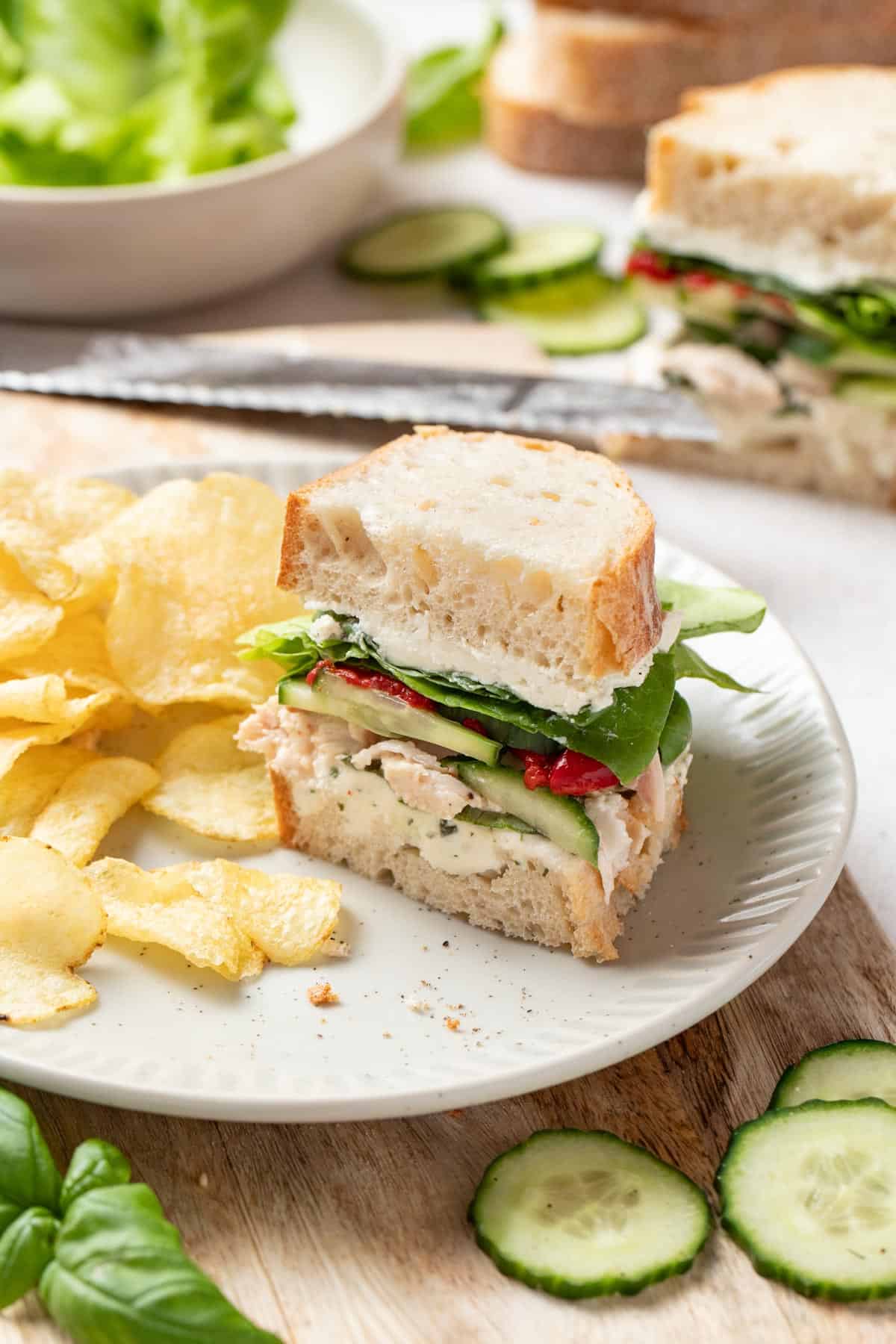 A sandwich sliced in half to show the inside next to potato chips on a plate.