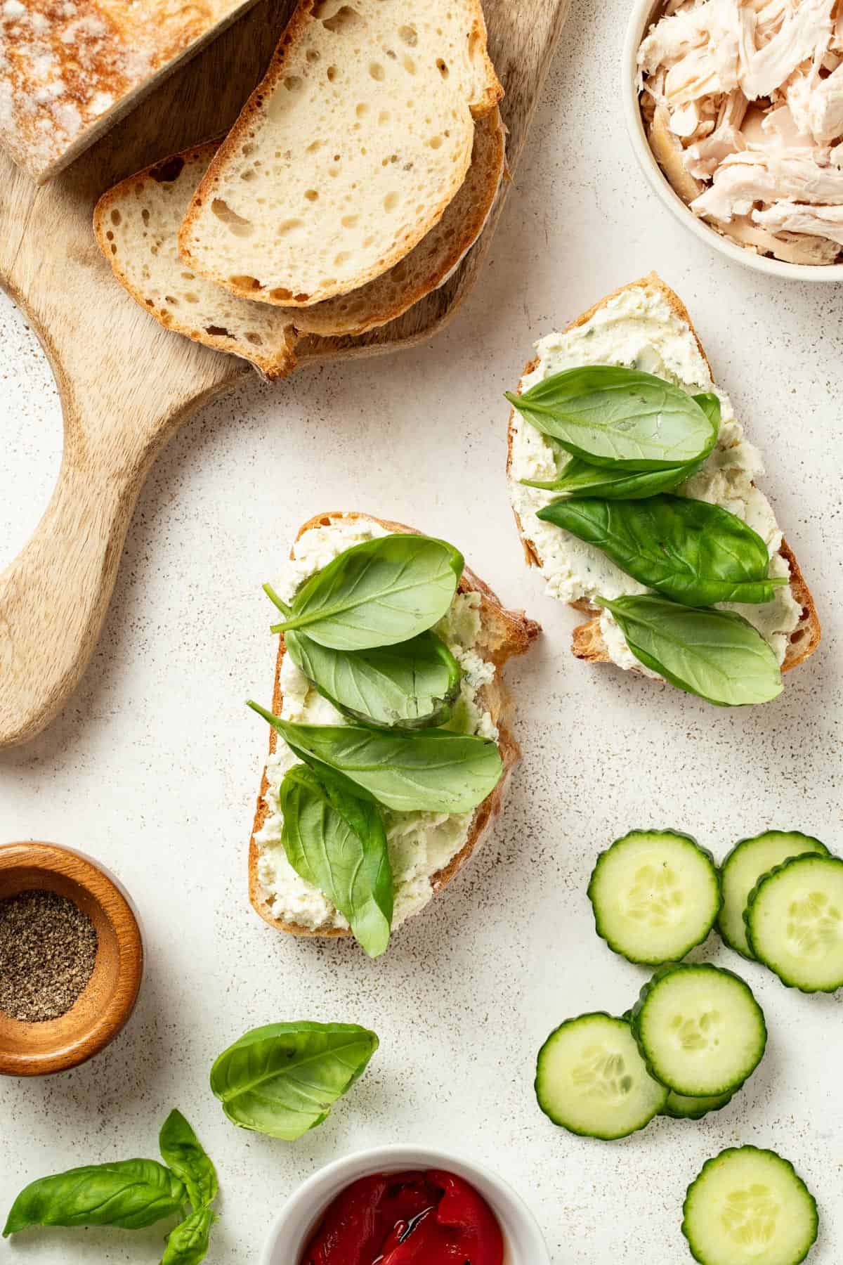 Adding fresh basil leaves on top of the Boursin cheese to the sandwich.