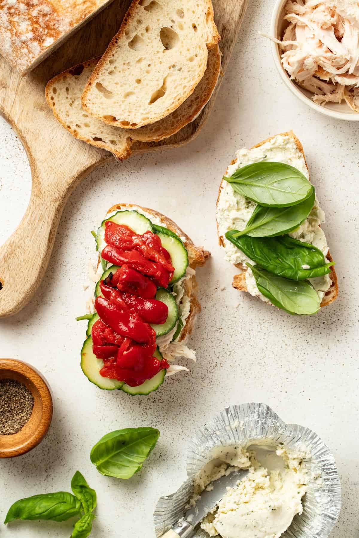 Adding cucumbers and roasted red peppers onto the top of the sandwich.