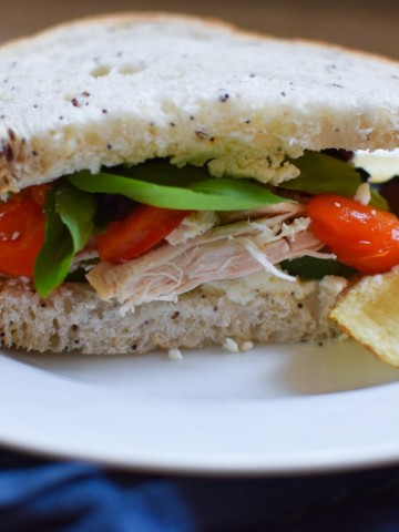 Sandwich with tomatoes, chicken, and spinach on a plate with chips