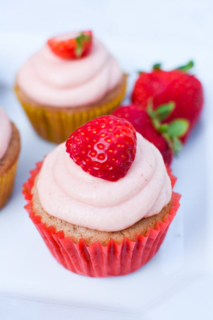 Gluten free strawberry cupcake with pink frosting in a red cupcake holder on a white plate.