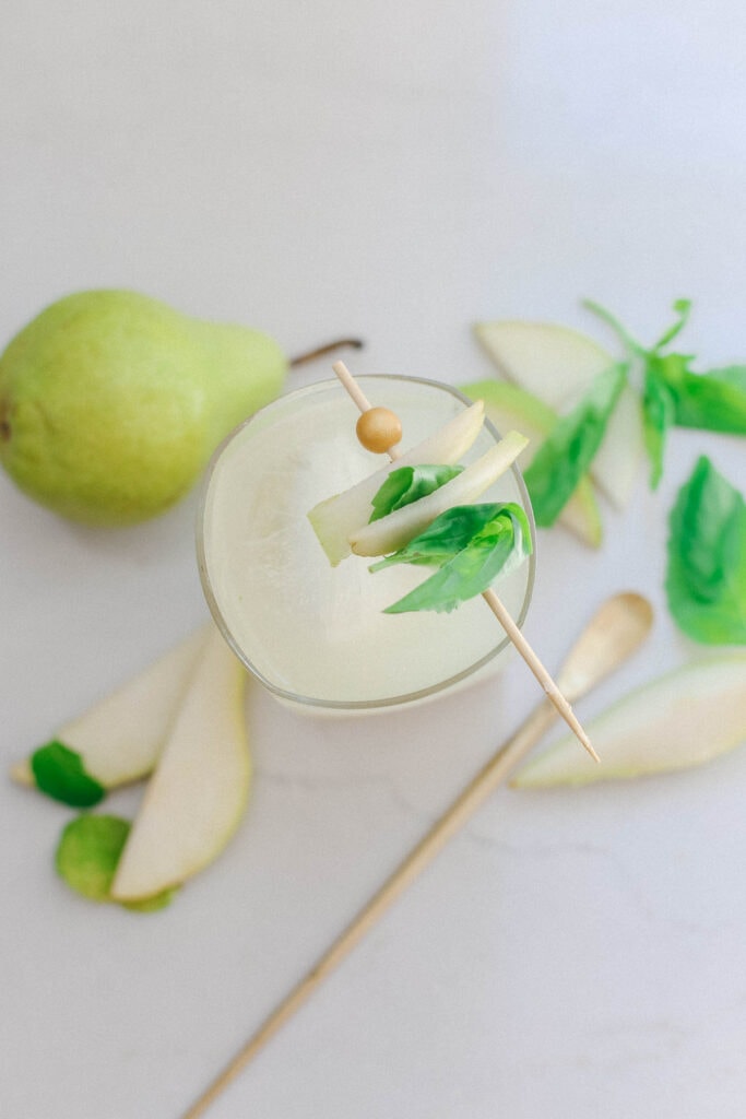 An overhead shot of a pear mocktail with a cocktail pick with pears, basil, and mint on top.
