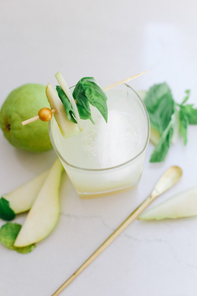 A mocktail topped with basil and mint on top of a white table.