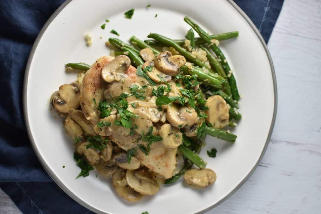 Chicken marsala on a grey plate topped with mushrooms on a white wood background