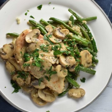 Chicken marsala on a grey plate topped with mushrooms on a white wood background