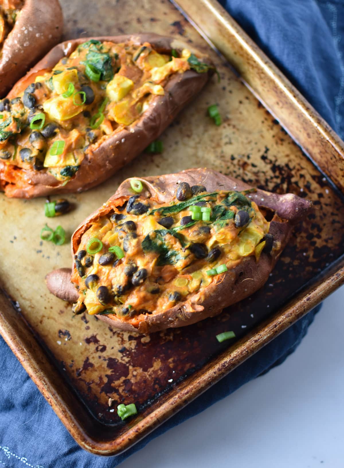 A stuffed sweet potato with Mexican-style filling topped with enchilada sauce on a baking sheet