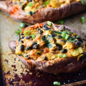 A mexican stuffed sweet potato on a sheet pan topped with green onion slices
