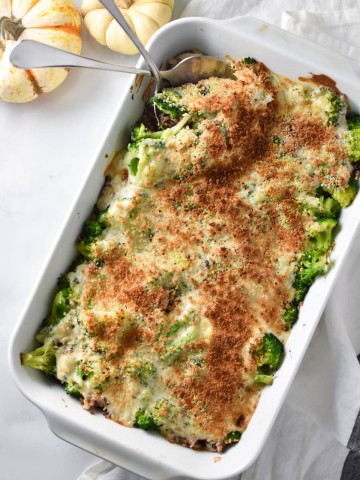 Serving spoons sticking into a broccoli rice casserole on a white surface