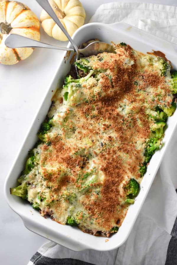 Serving spoons sticking into a broccoli rice casserole on a white surface