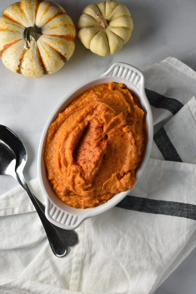 whipped sweet potatoes in an white gratin dish next to small pumpkins