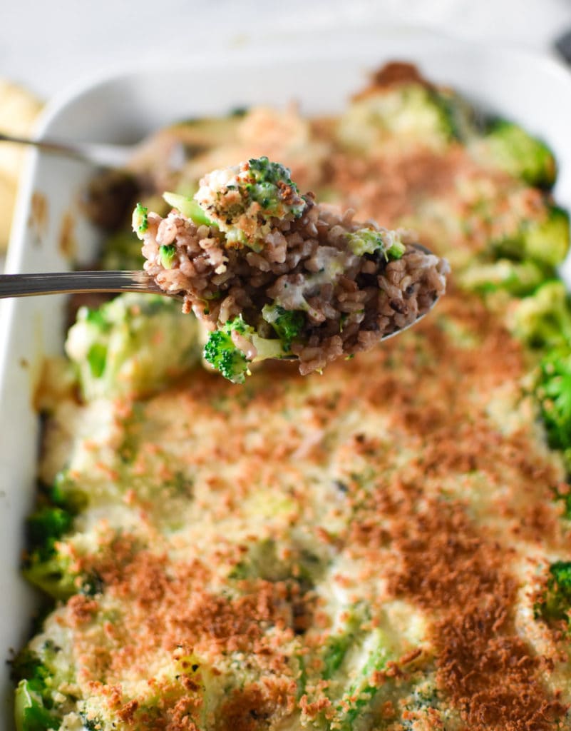 A scoop of broccoli rice casserole in a spoon with the casserole in the background