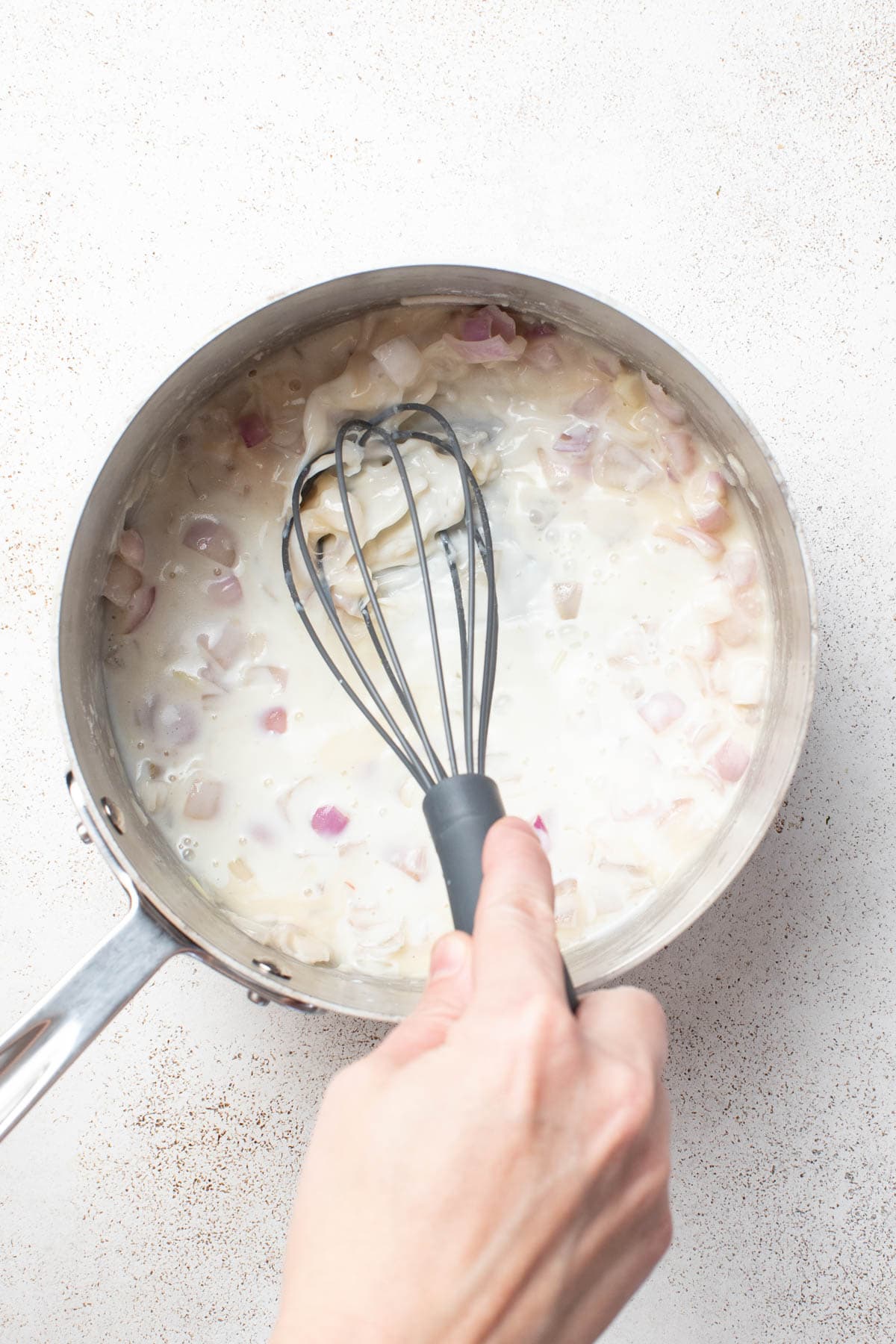 Stirring the Boursin cheese sauce with a whisk to smooth it out.